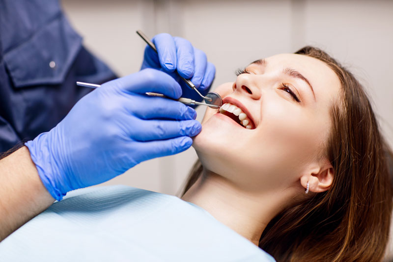 an image of a woman smiling in patient seat as a dentist cleans her teeth